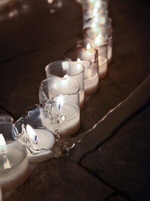A line of lit votive candles, one is broken
