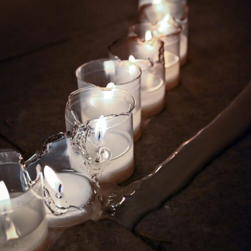 A line of lit votive candles, one is broken